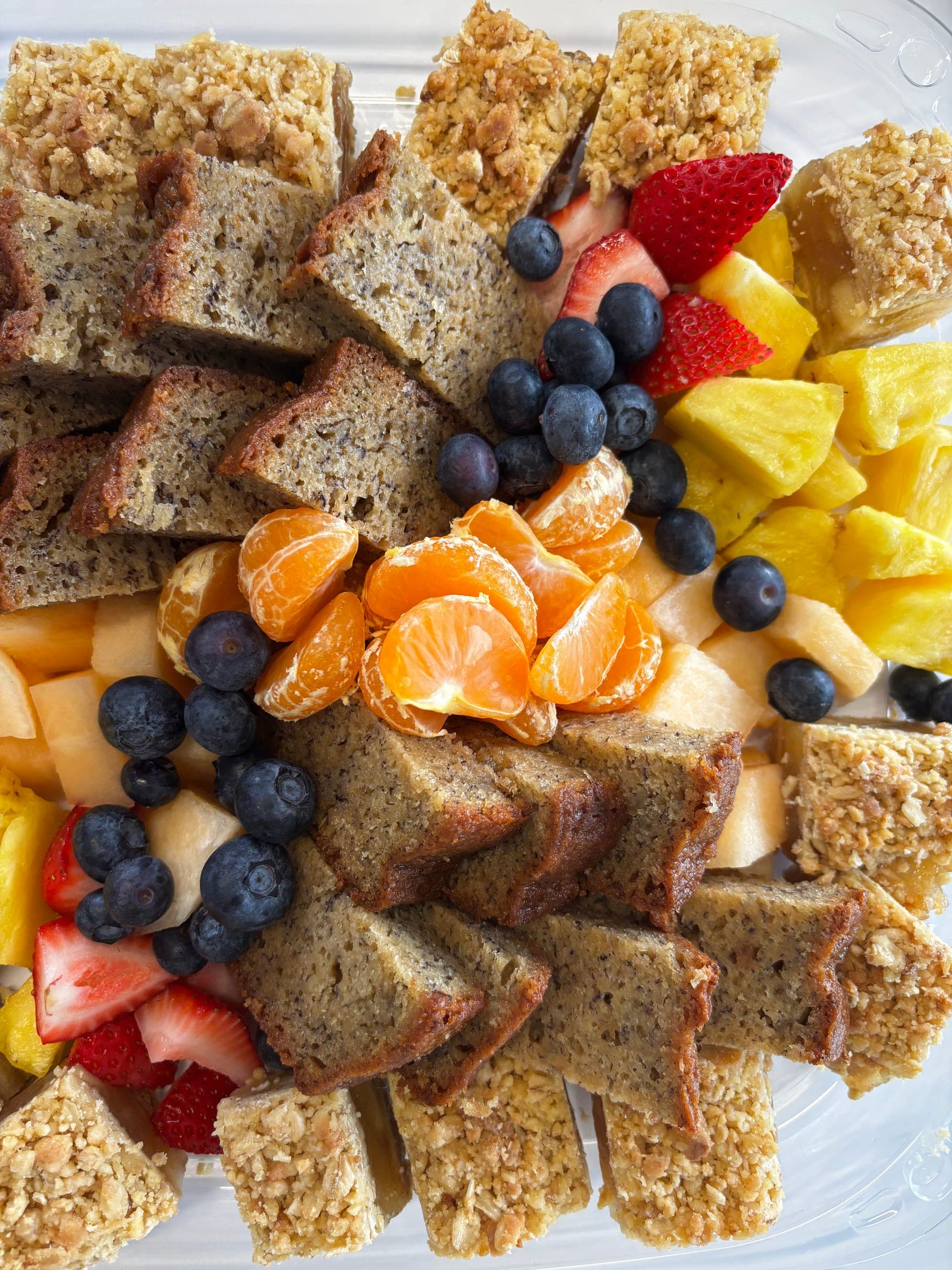 Breakfast platter of banana bread, oat squares, orange segments, pineapple and fresh berries