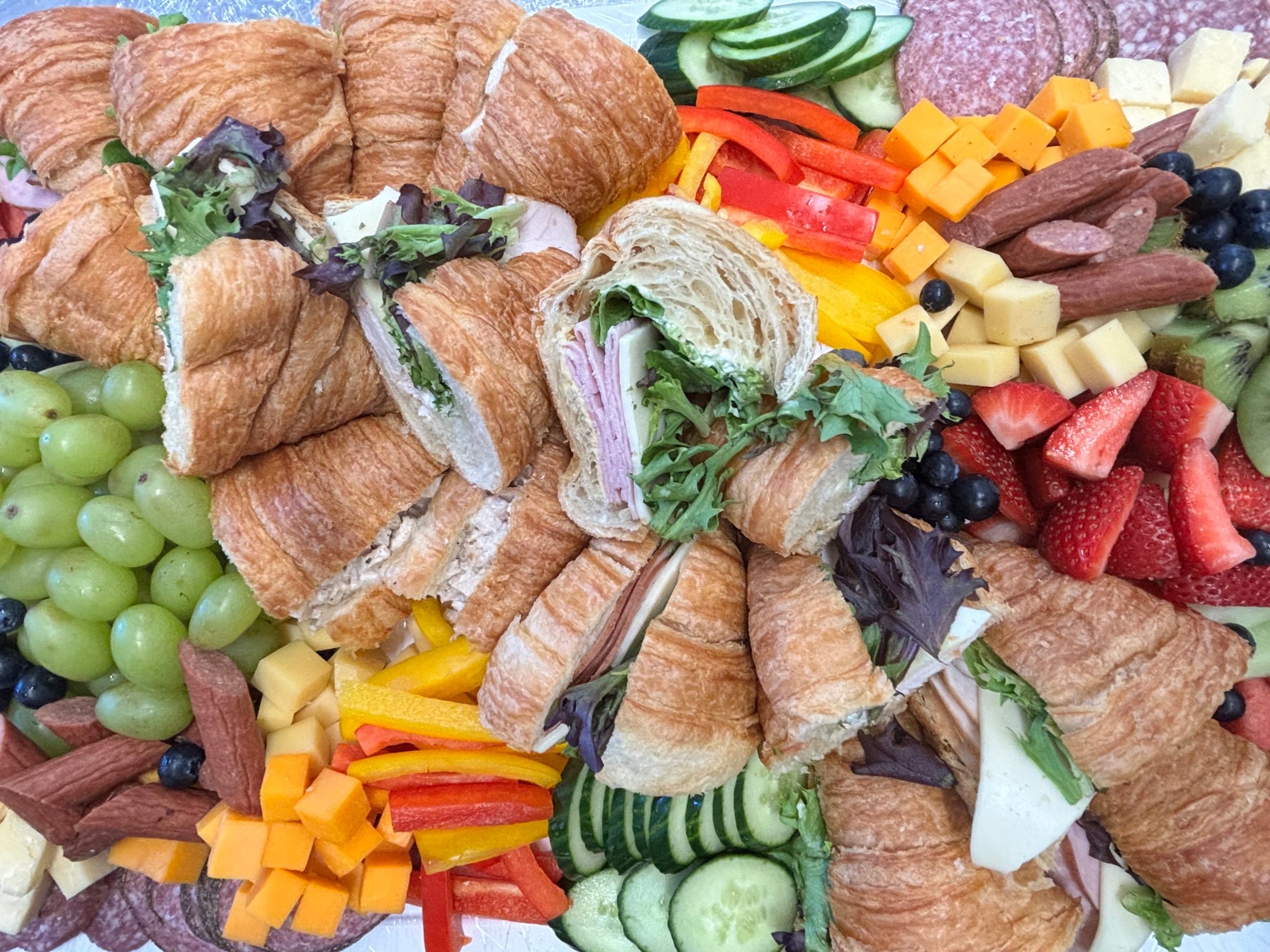 Catering platter of croissant sandwiches with fresh fruit, vegetables, cheese and sliced meats