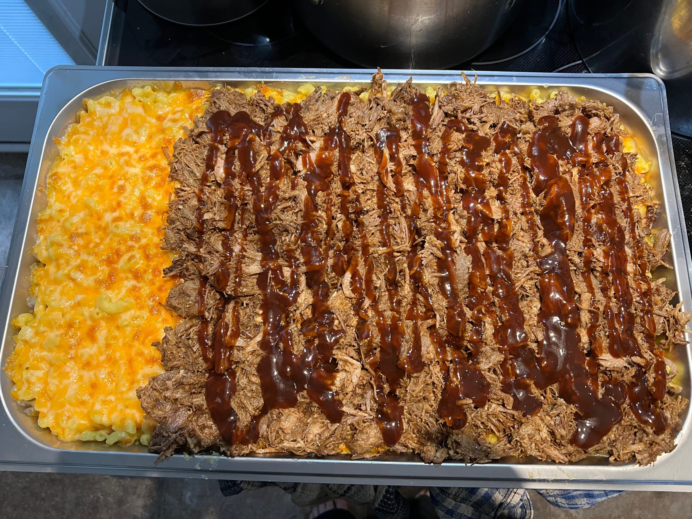 Catering tray of saucy pulled pork served over baked macaroni and cheese