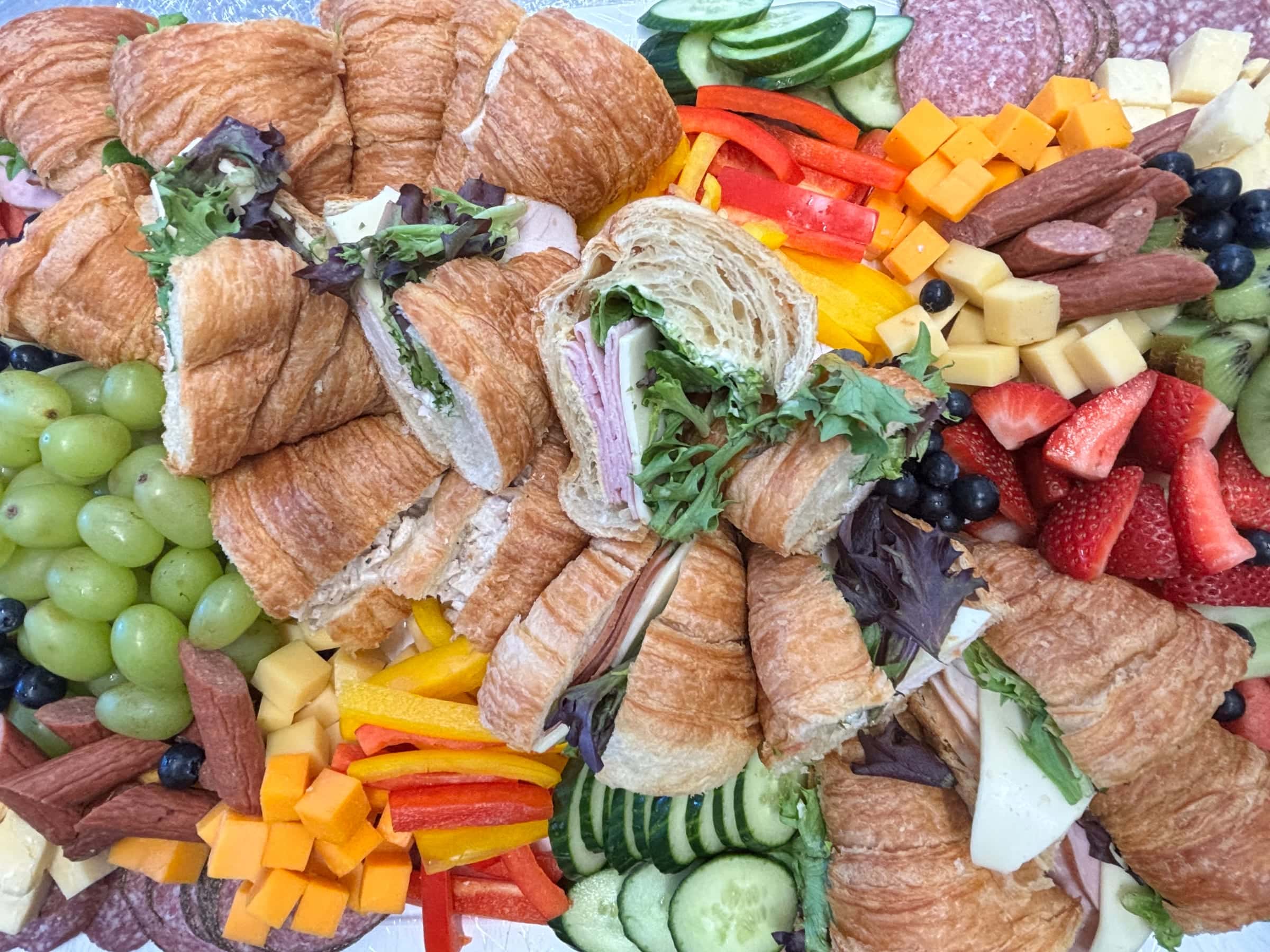 Catering platter of croissant sandwiches with fresh fruit, vegetables, cheese and sliced meats