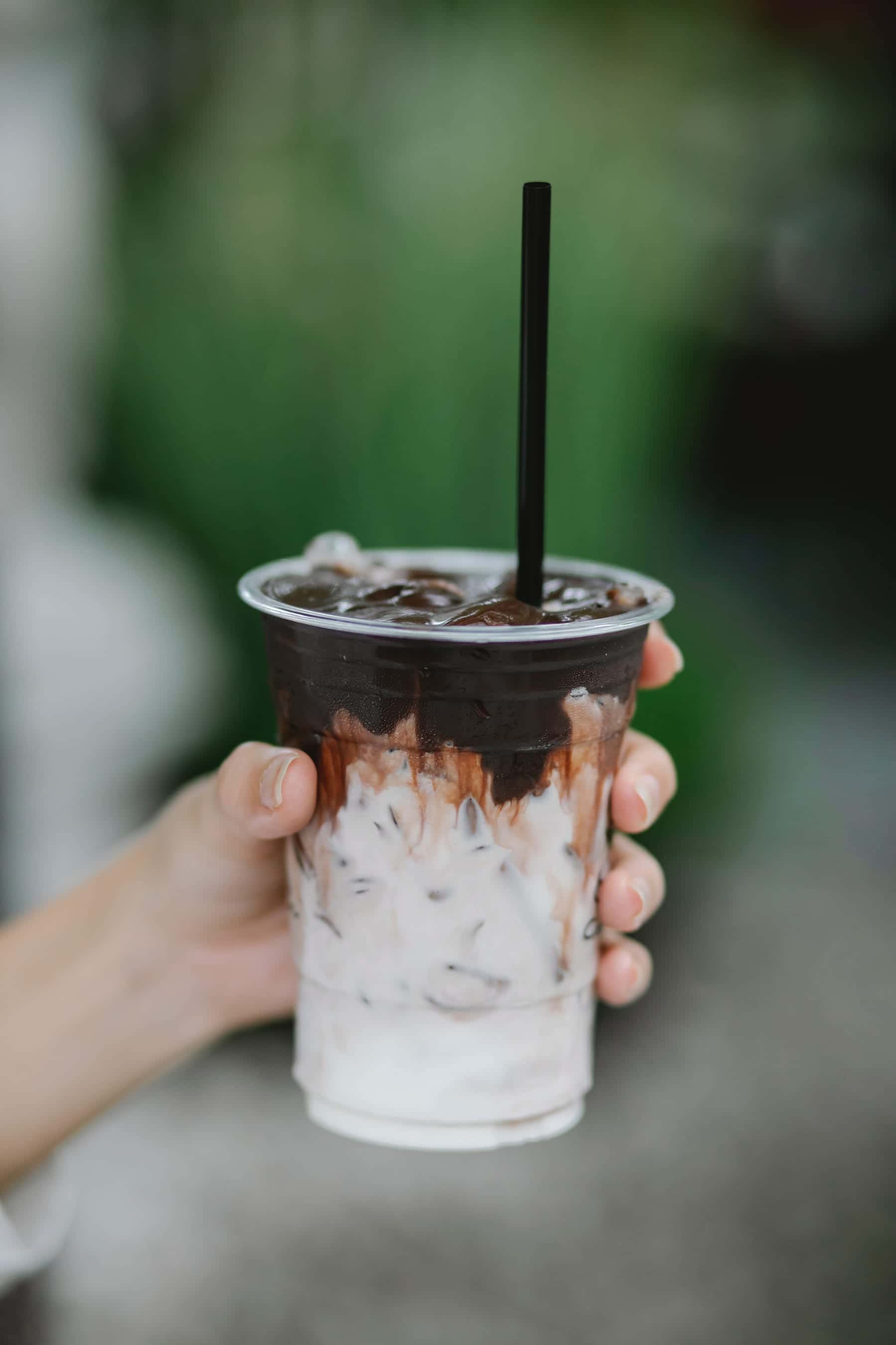 Hand holding an iced mocha in a clear cup with a straw